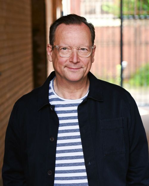 Nahaufnahme-Porträt des Schauspielers Matthias Brandt mit schwarzer Brille und gestreiften Shirt
