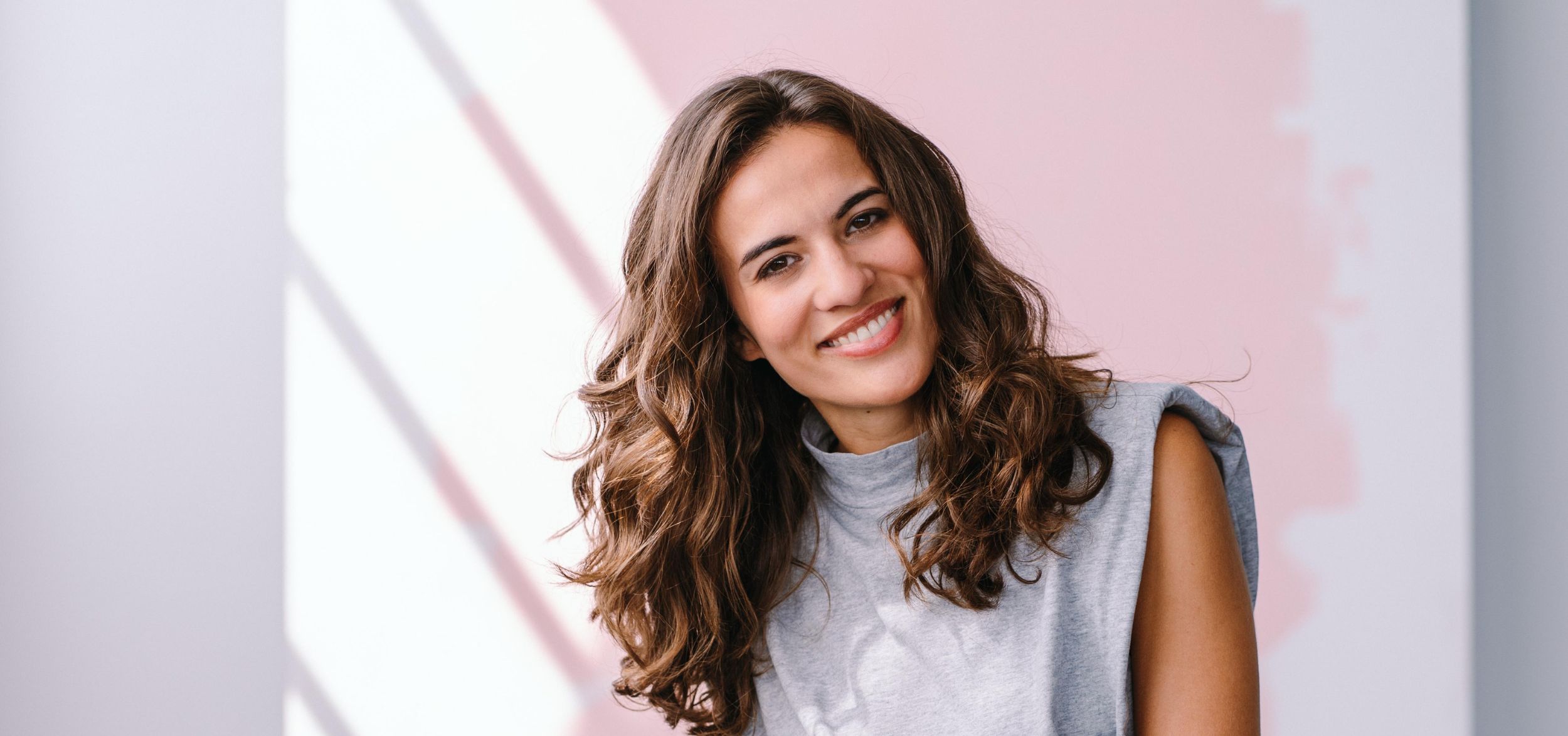 Mona Ameziane Lächeln zur Kamera Halbporträt Hintergrund helle rosafarben